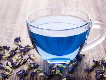 A cup of Butterfly Pea Flower Tea featuring its striking blue color, surrounded by dried Clitoria ternatea petals.