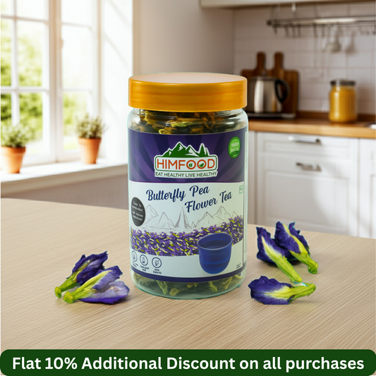 Himalayan butterfly pea flower tea 25g jar on kitchen counter with blue butterfly pea flowers nearby.